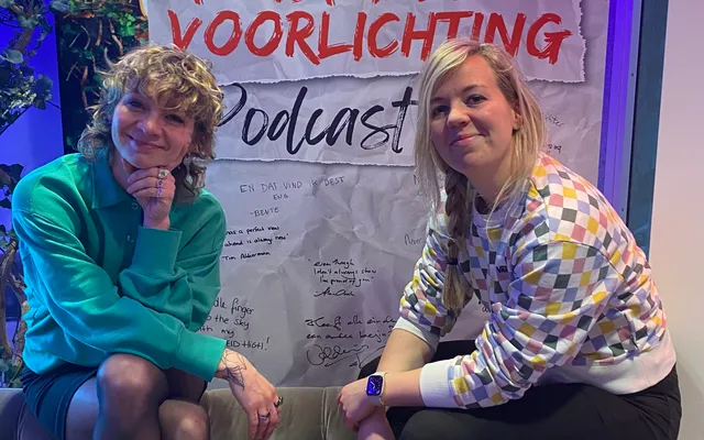 Martine ten Klooster in gesprek met Jacqueline Govaert voor de muur met daarop Tekstuele voorlichting Podcast.