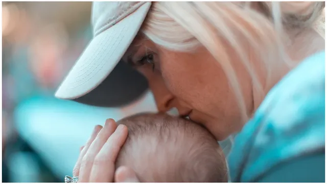 Oudere vrouw kust baby op het hoofd om een moeder van 45 jaar of ouder met kind te illustreren. Nieuwlicht over keerzijde moeder worden na 45 jaar.