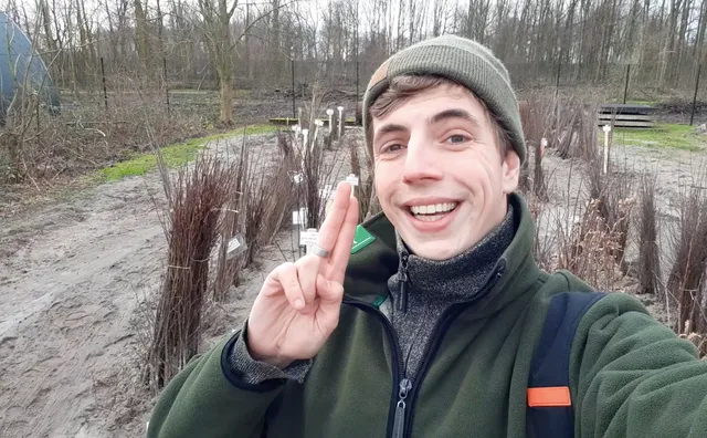 Boswachter Jonathan met twee vingers in de lucht bij een zandtuin met takken.